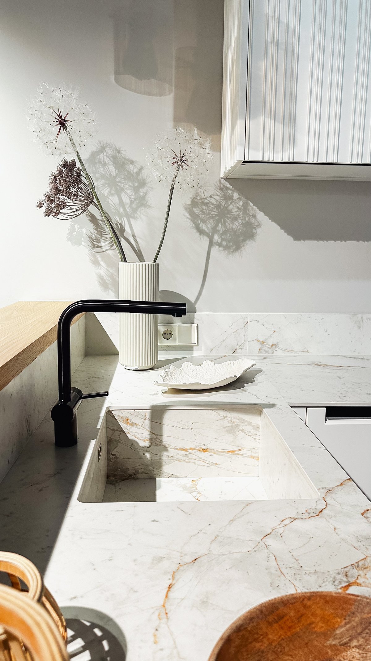 Contemporary kitchen interior featuring marble countertop with black faucet and sunlight shadows