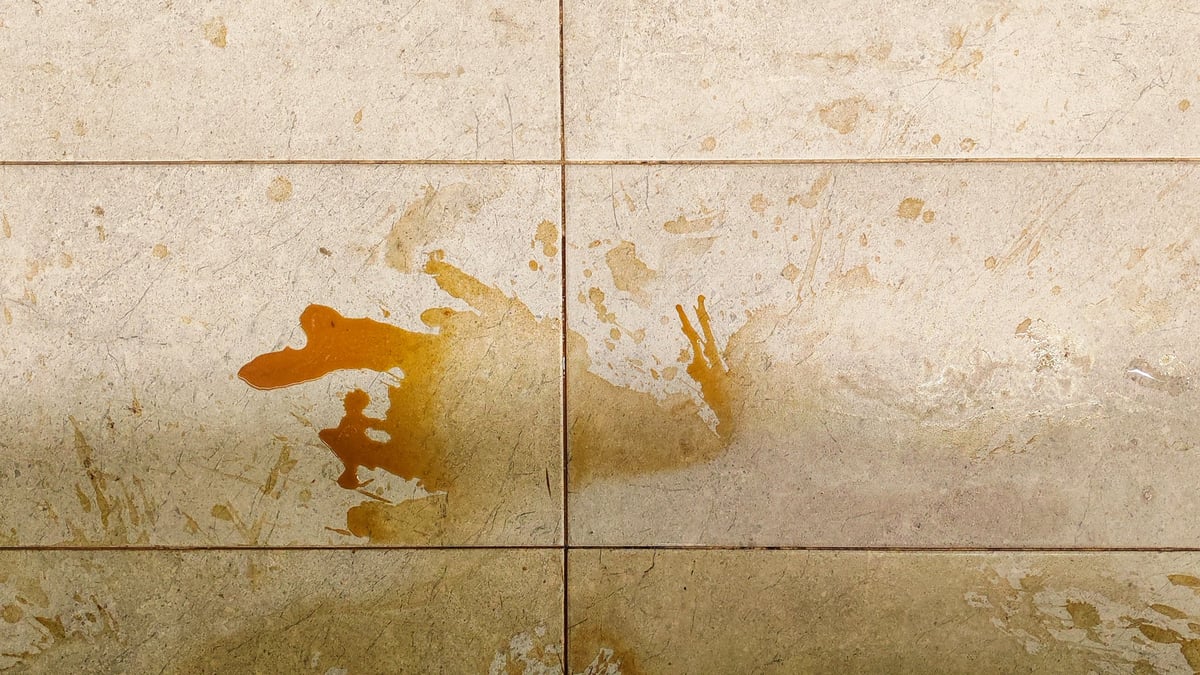 Brown liquid spilled on floor tiles — stain damage on stone surface requiring cleaning